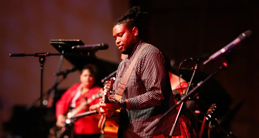 a black man playing guitar and performing on stage at event
