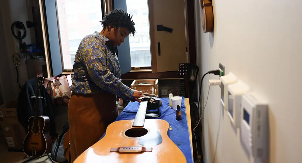 a young black woman cleaning a guitar in the Luthiery