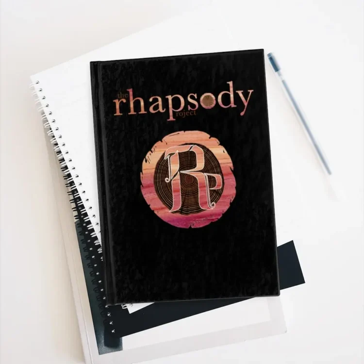 The Rhapsody Project Journal sitting on top of other notebooks with pen