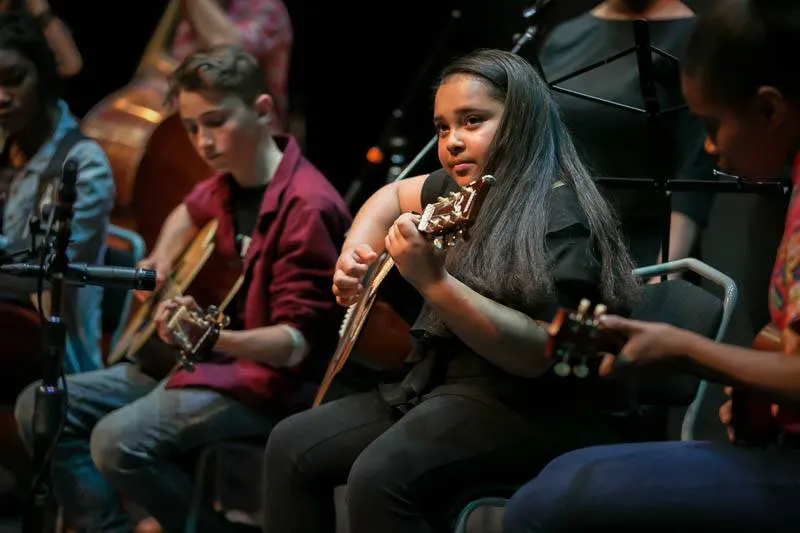 a young girl playing guitar youth program