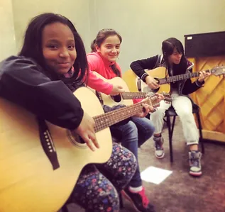 three girls playing guitar smiling