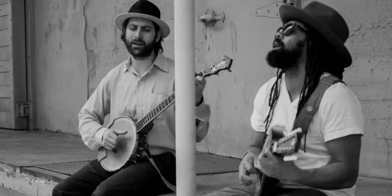 Black and white photo of Joe Seamons and Ben Hunter seated on a porch singing and playing banjo and mandolin.